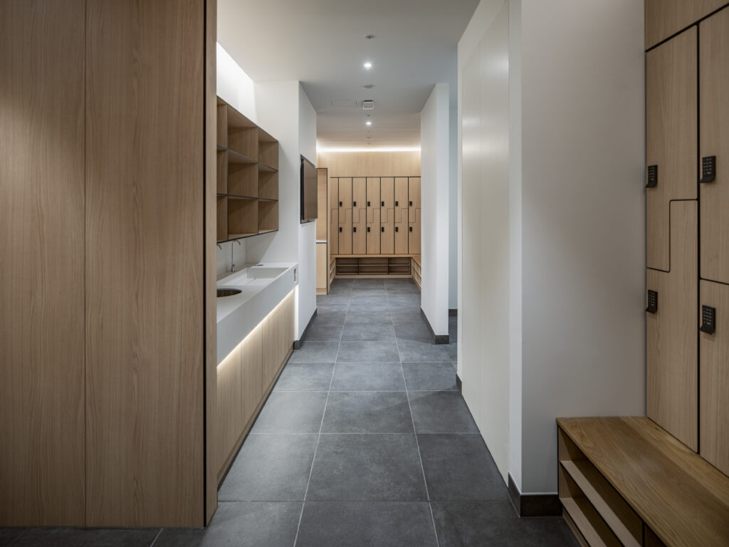 Changing room at YY London with timber lockers, a vanity unit and grey stone flooring