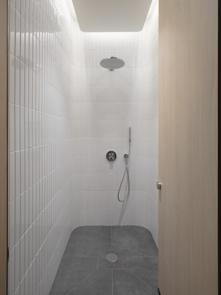 Shower cubicle at YY London's end-of-trip facilities with a rainfall showerhead and white tiling