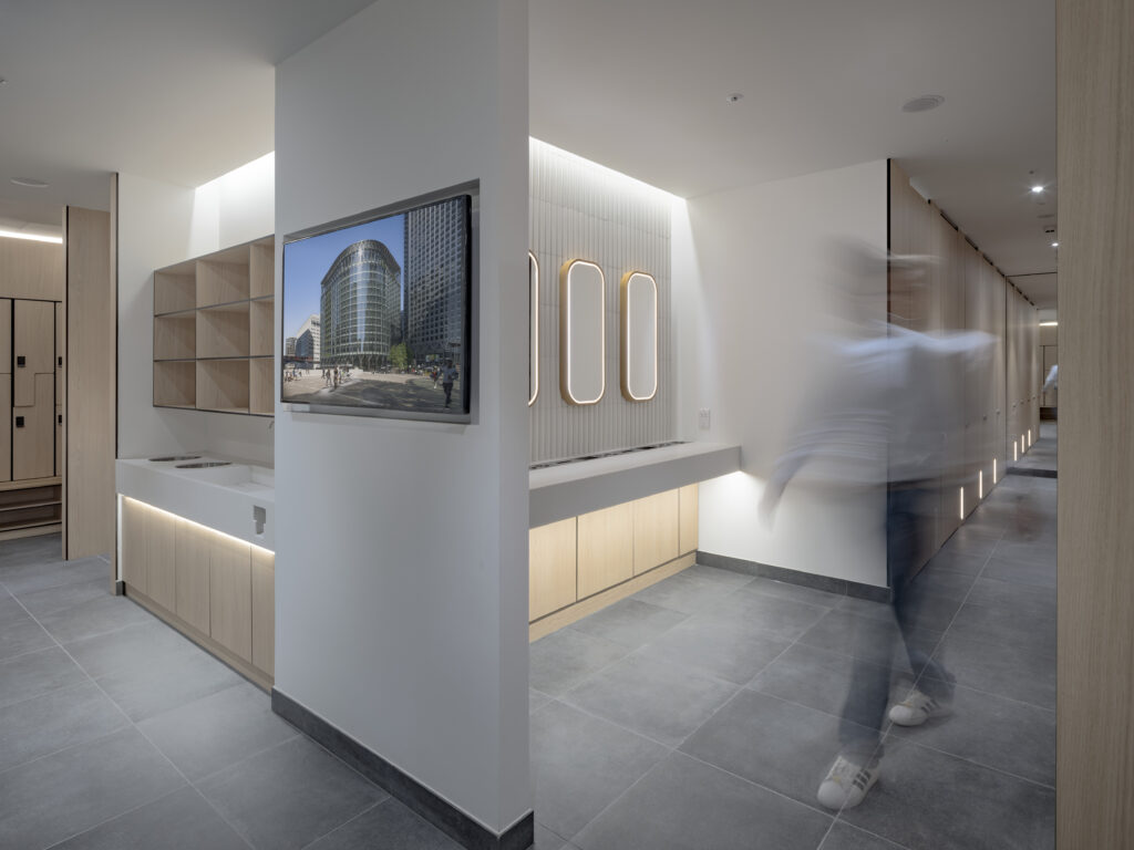 Corridor at YY London with a wall-mounted screen displaying a building image and timber lockers beyond
