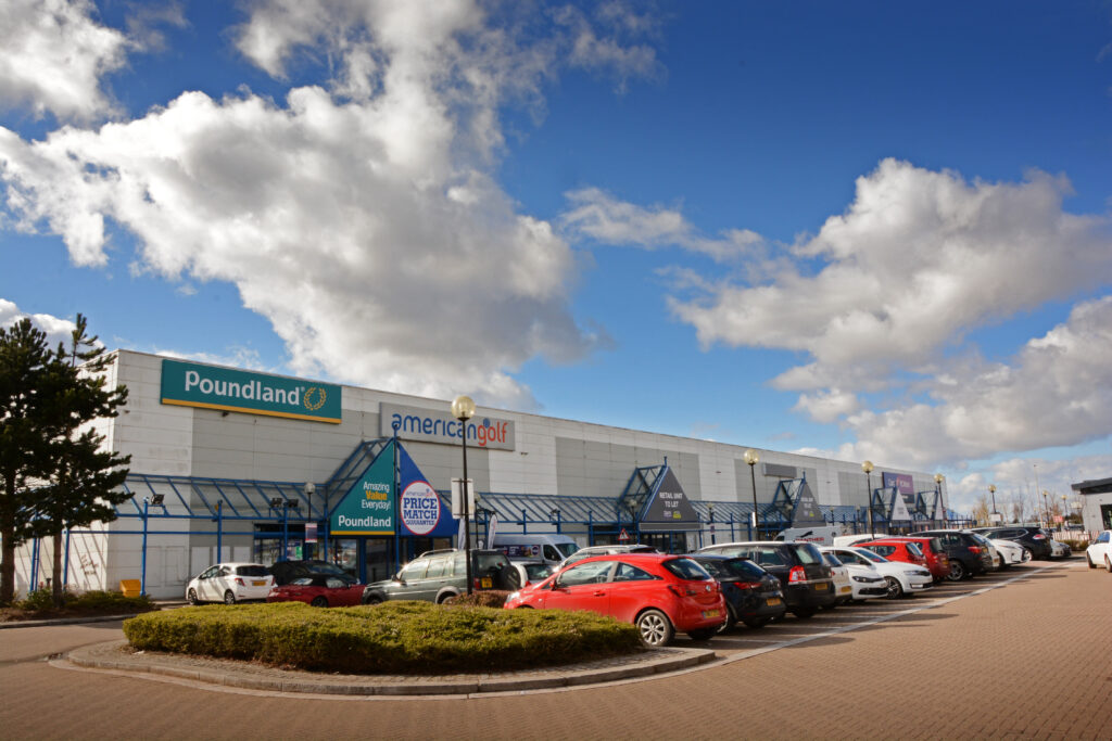 Retail units including Poundland and American Golf at The Place Retail Park under a cloudy sky