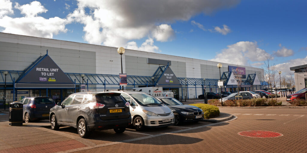 Vacant units with 'Retail Unit To Let' signage and car park at The Place Retail Park