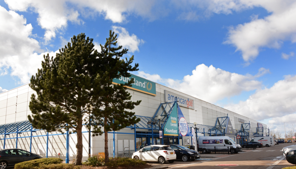 The Place Retail Park unit fronts including Poundland and American Golf, with car park in foreground