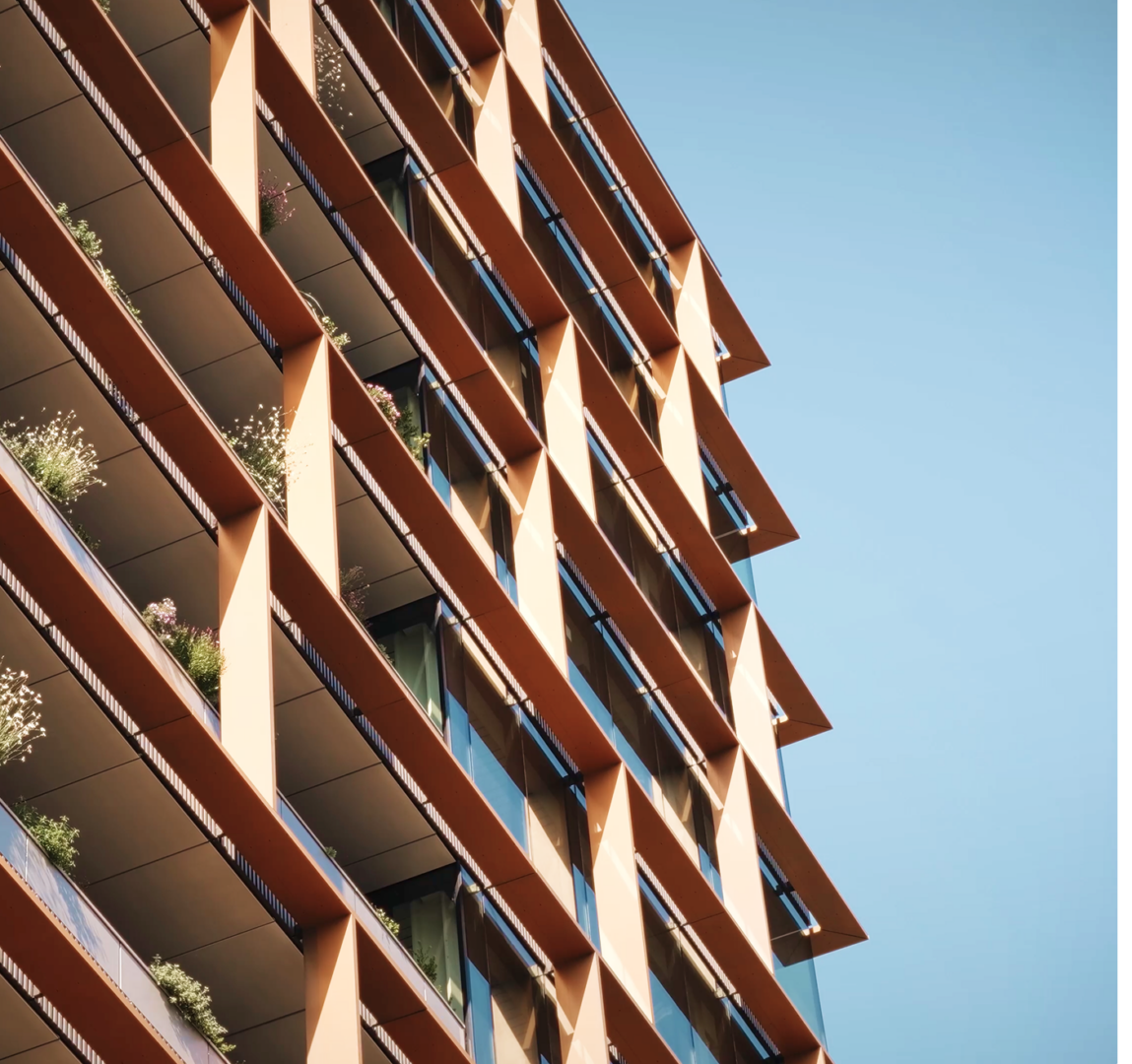 Close-up of a residential tower's angular bronze balcony fins with planting, set against a blue sky