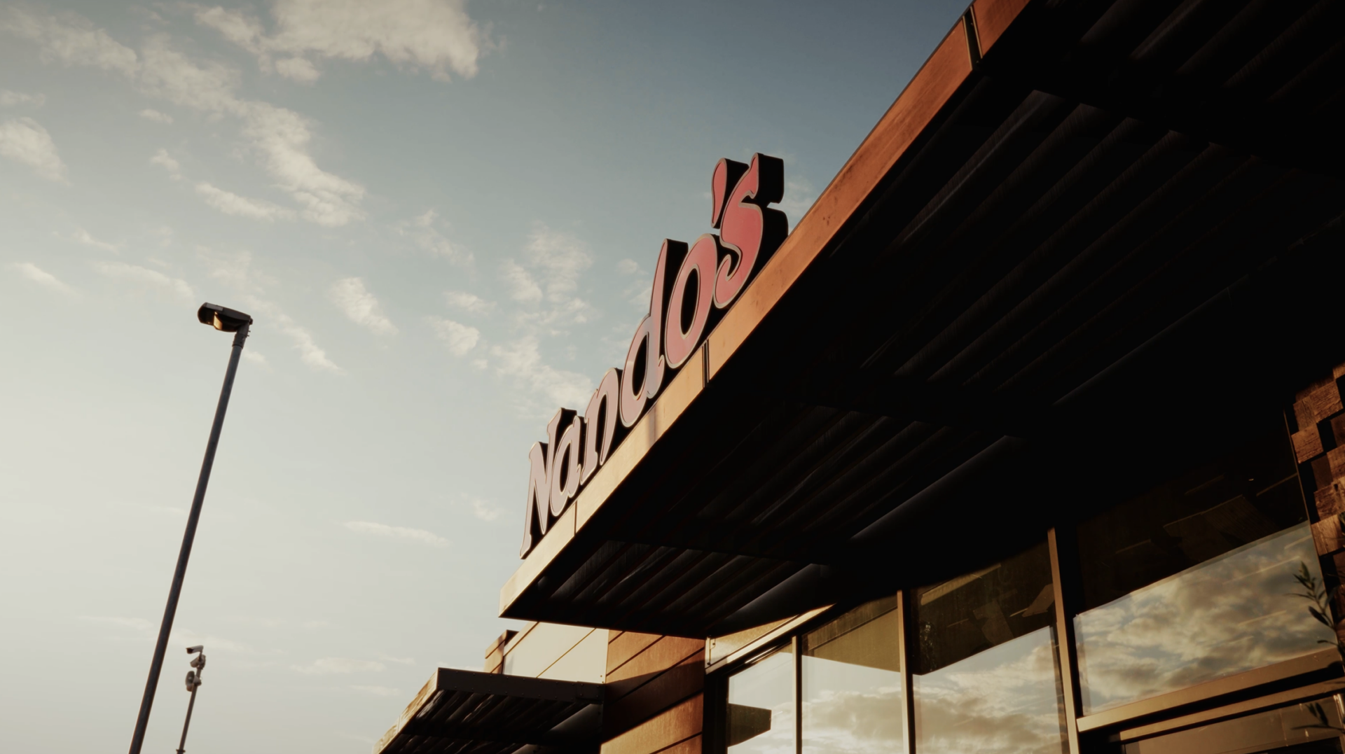 Nando's restaurant signage on a retail unit canopy at dusk