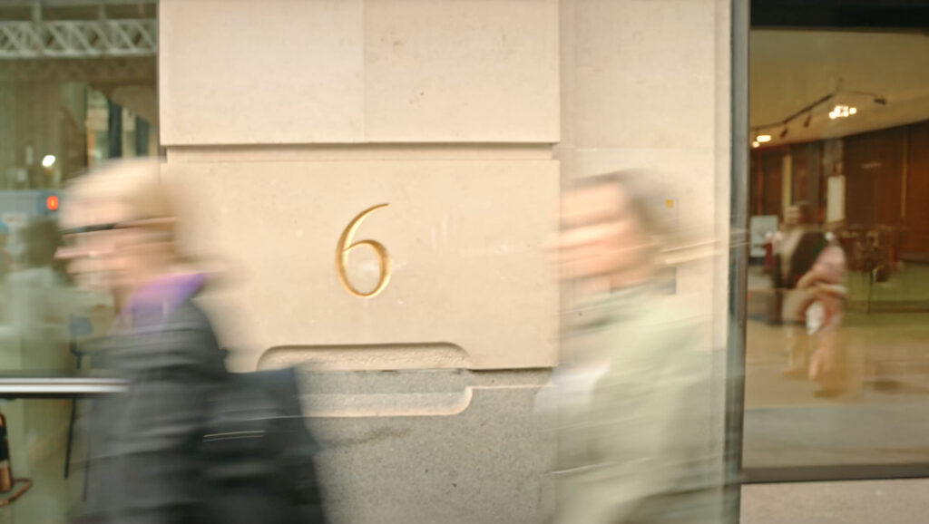 Gilded number 6 carved into the stone entrance pier at 6 Gracechurch Street, with pedestrians passing