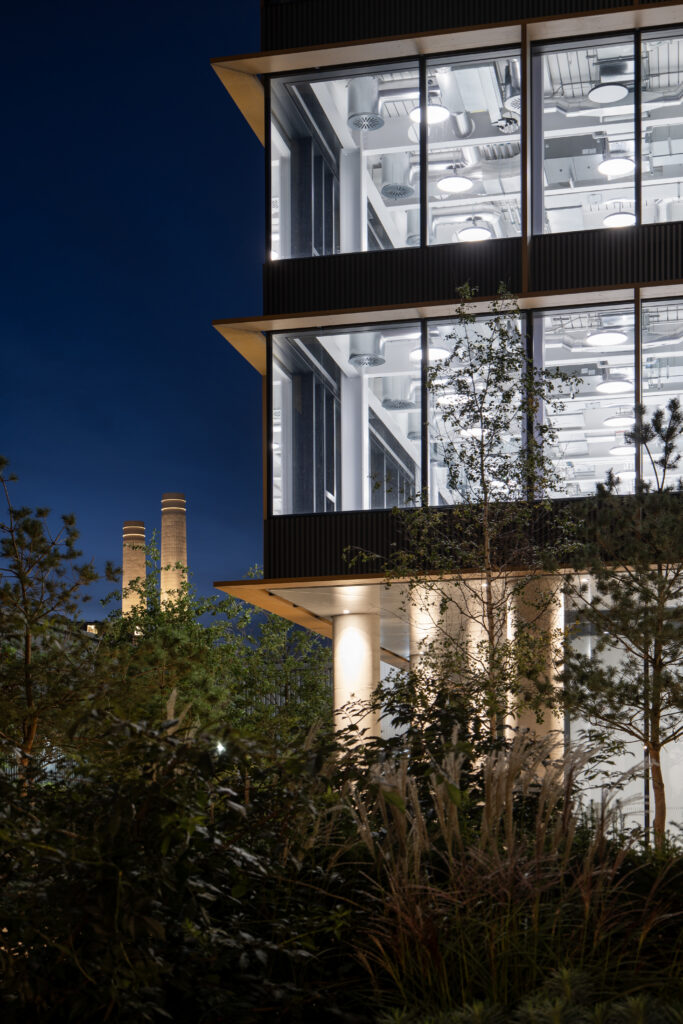 Osmo Nine Elms lit at night, with Battersea Power Station's chimneys beyond the planting
