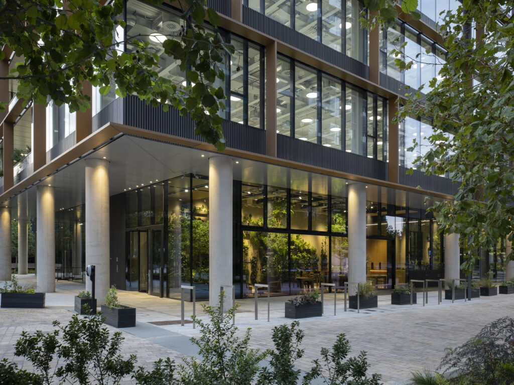 Colonnaded ground-floor entrance at Osmo Nine Elms at dusk, with planting and outdoor seating